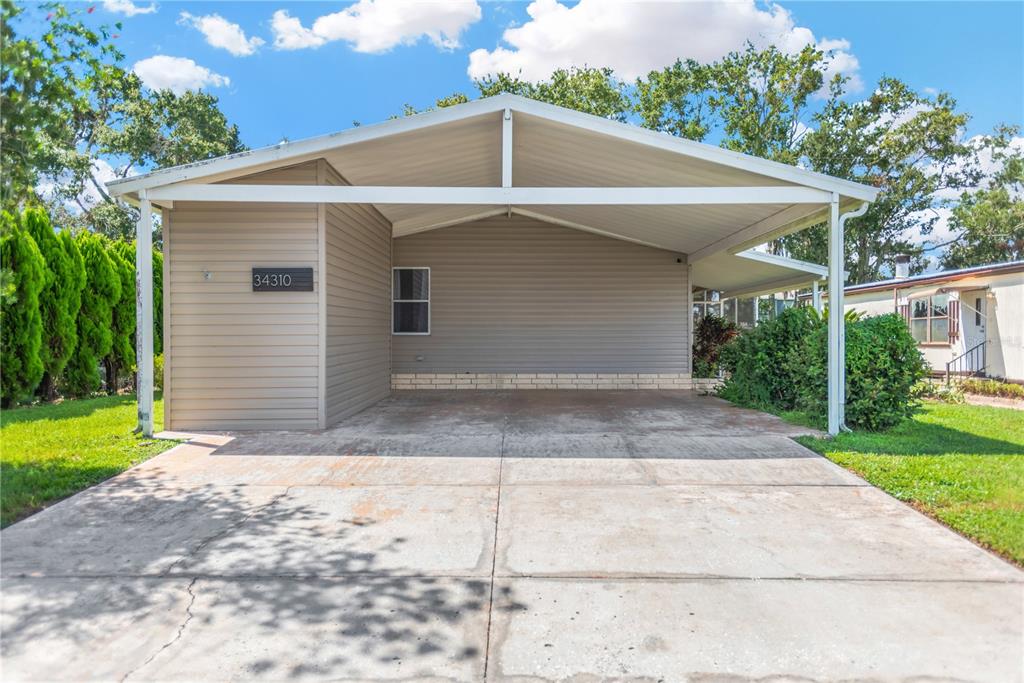 A beige house exterior features a large attached carport over a concrete driveway — 34310 LODGE DRIVE, WESLEY CHAPEL, FL
