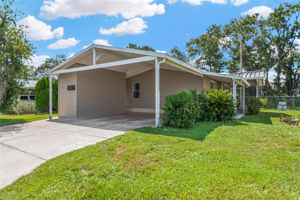 A single-story house with a carport, tan siding, and a green lawn under a blue sky — 34310 LODGE DRIVE, WESLEY CHAPEL, FL