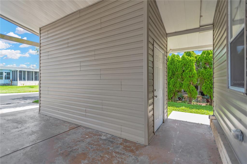 A covered concrete carport features a beige vinyl-sided storage shed with a white door — 34310 LODGE DRIVE, WESLEY CHAPEL, FL