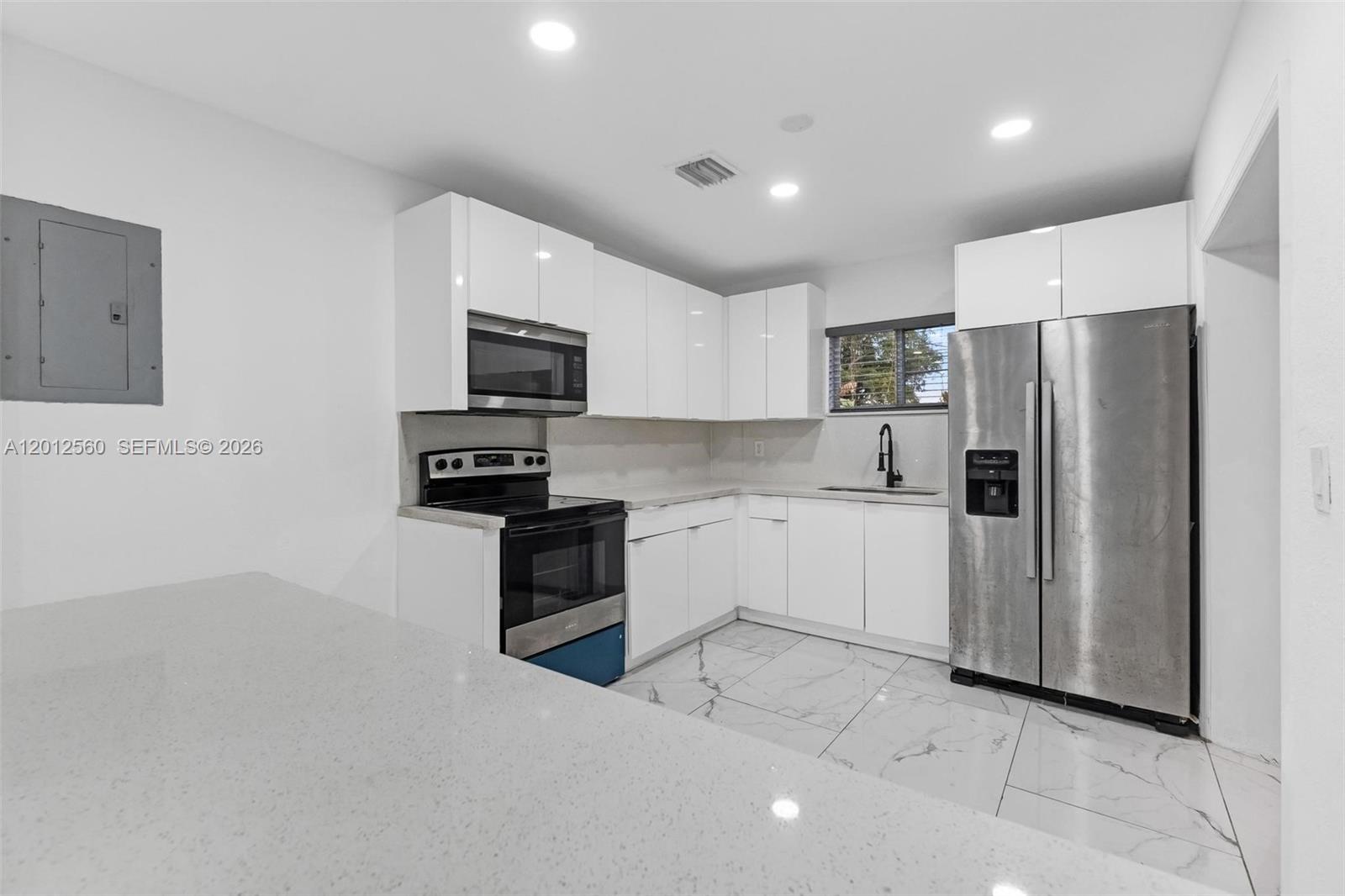 A modern kitchen features white cabinets, stainless steel appliances, and light-colored marble-patterned tile floors — 4530 SW 25th St, West Park FL 33023, WEST PARK, FL