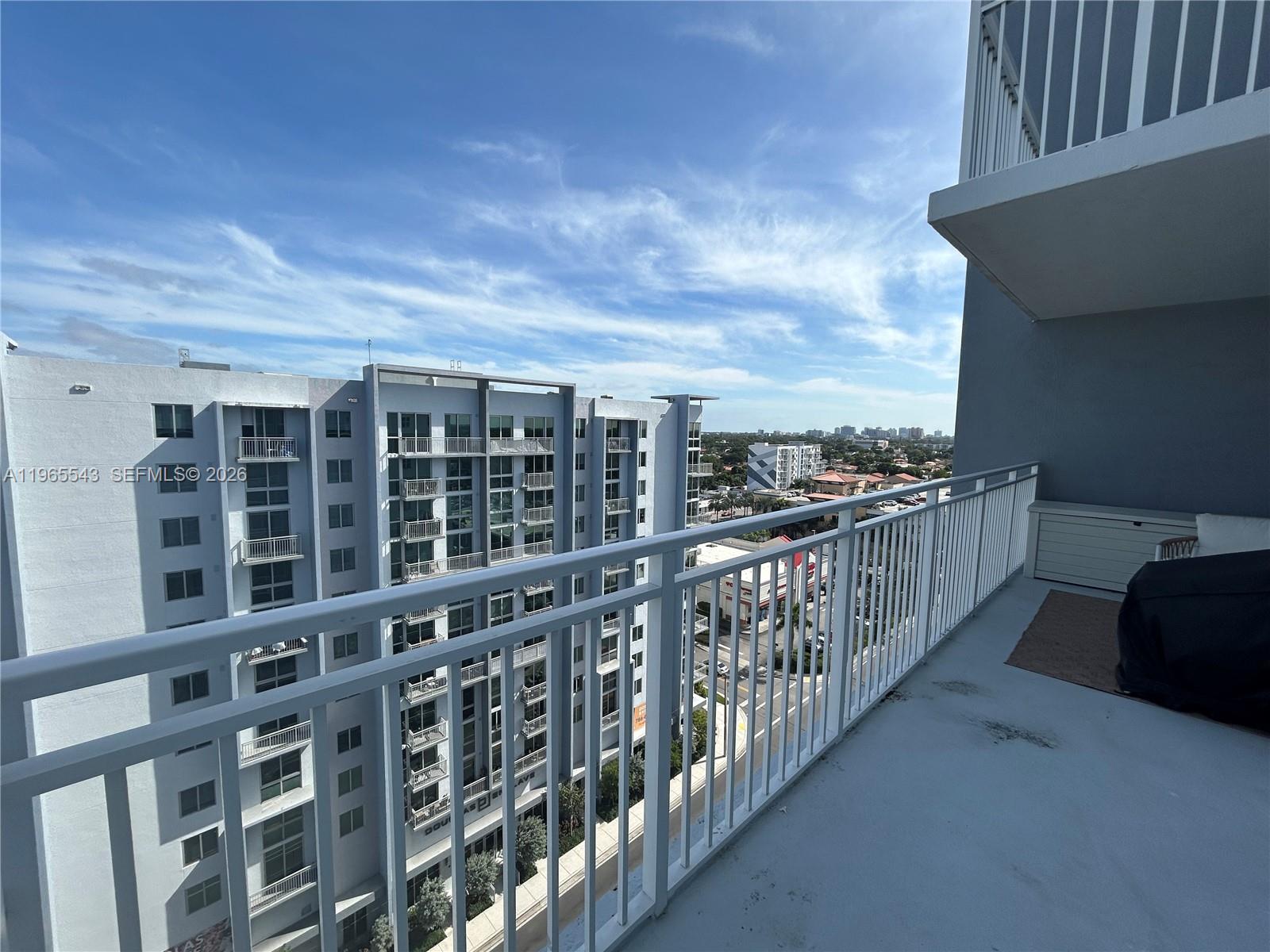 A high-rise balcony with a white metal railing overlooks a neighboring apartment building and street — 60 NW 37th Ave # 1205, Miami FL 33125, MIAMI, FL