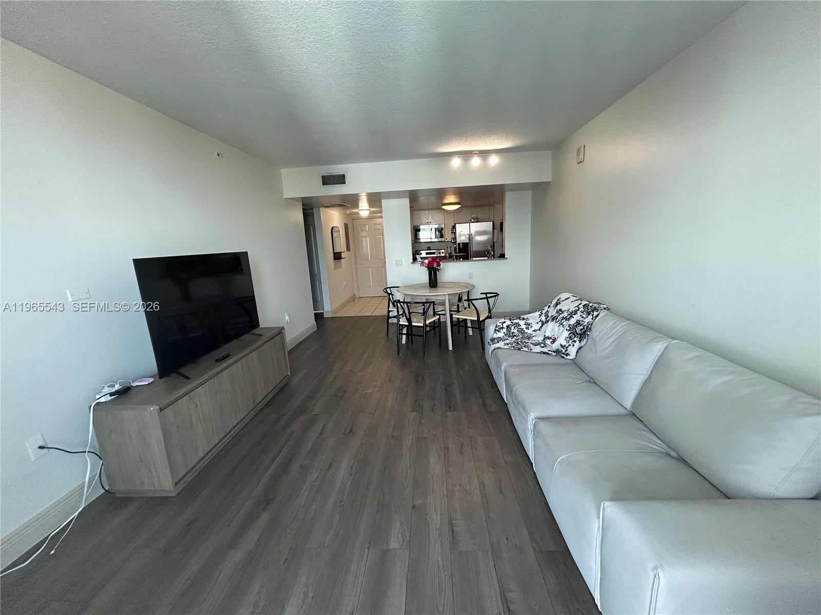 A living room features gray wood-look flooring, a white sofa, and a dining area — 60 NW 37th Ave # 1205, Miami FL 33125, MIAMI, FL
