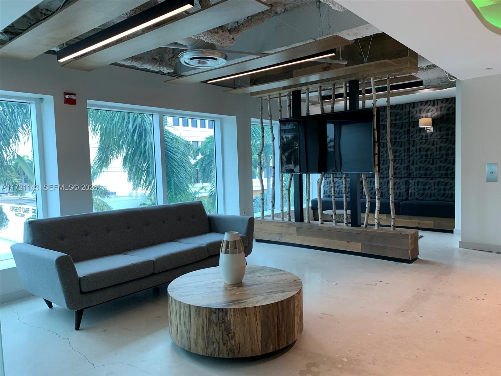 A modern lounge features a gray sofa, a wood-stump coffee table, and a birch-pole partition — 820 W 41 St # 401, Miami Beach FL 33140, MIAMI BEACH, FL