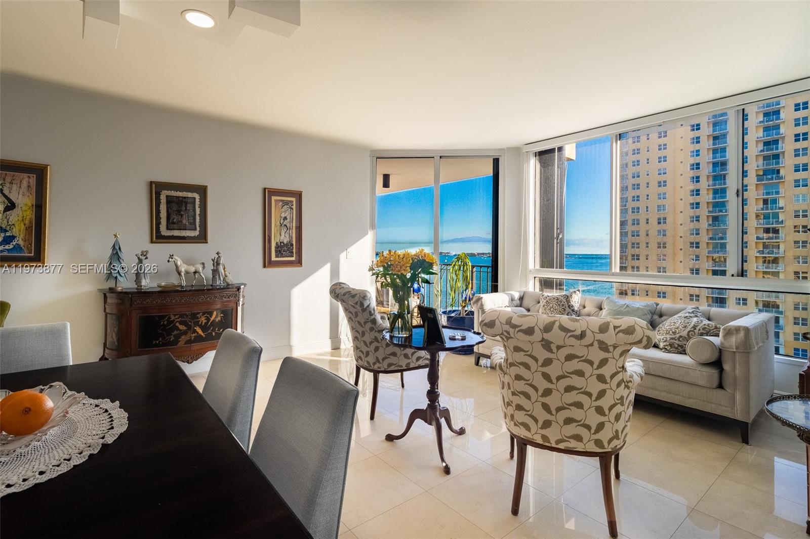A living and dining area features tile floors, patterned armchairs, and floor-to-ceiling windows overlooking the ocean — 520 Brickell Key Dr # A1007, Miami FL 33131, MIAMI, FL