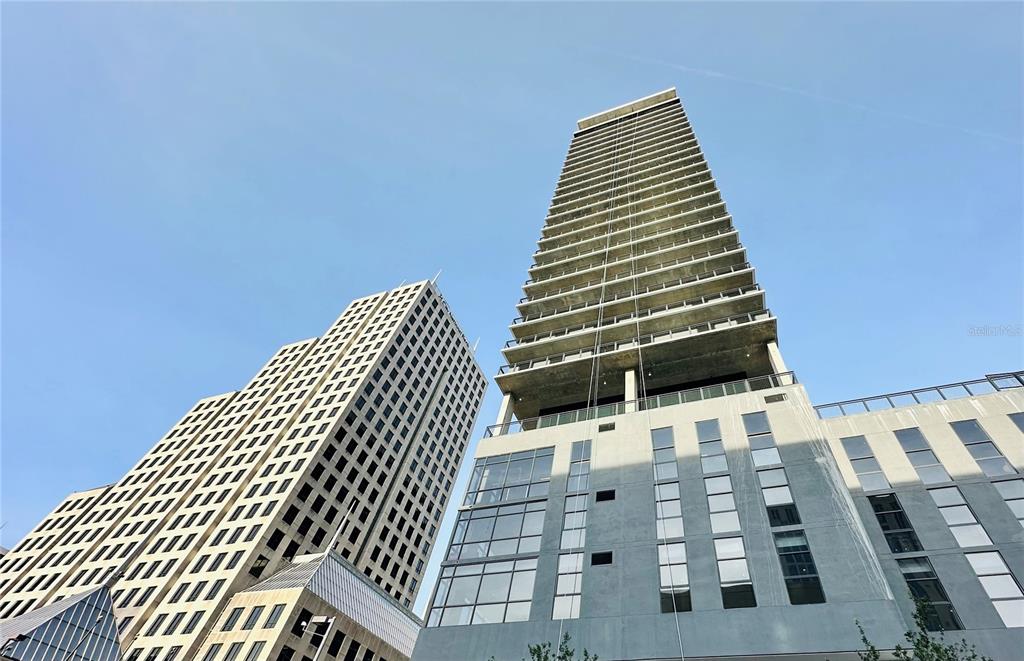 A low-angle view shows two modern high-rise buildings with glass and concrete facades against a blue sky — 434 N ORANGE AVENUE, ORLANDO, FL