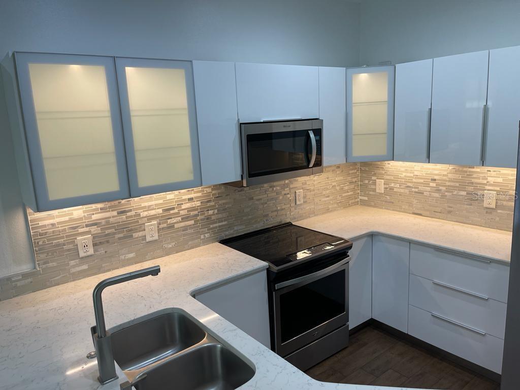 A modern kitchen featuring white cabinets, stainless steel appliances, and a tiled backsplash — 3153 CAPRI ISLE WAY, ORLANDO, FL