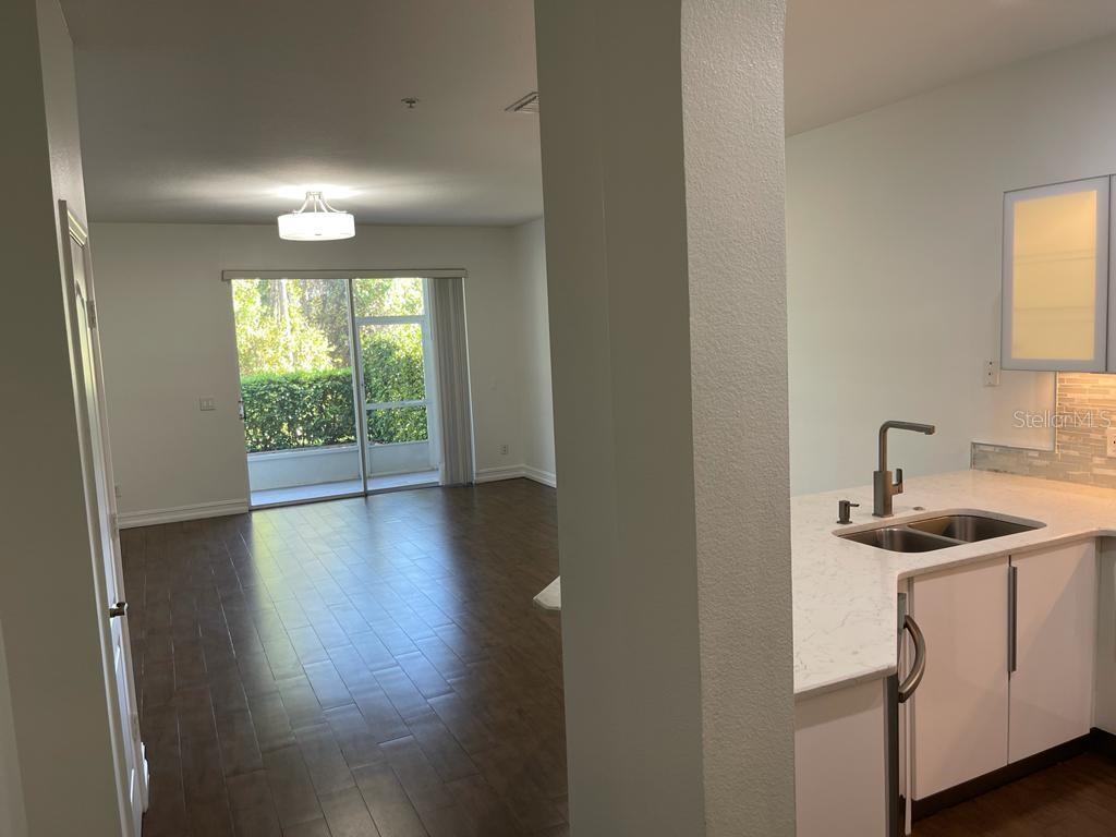 A view from a kitchen looking into a living room with wood floors and sliding doors — 3153 CAPRI ISLE WAY, ORLANDO, FL
