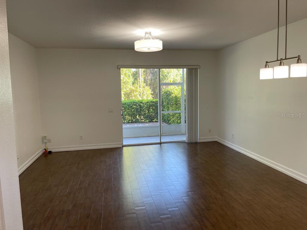 An empty living area features dark wood-look flooring, a sliding glass door, and two light fixtures — 3153 CAPRI ISLE WAY, ORLANDO, FL