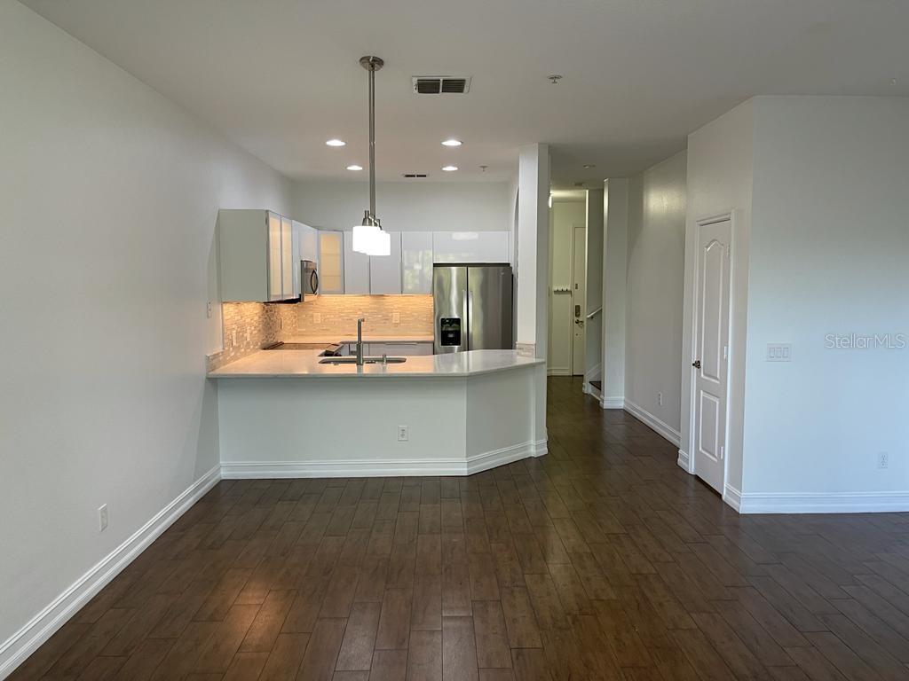A kitchen with white cabinets, stainless steel appliances, and a peninsula overlooks a wood-floored room — 3153 CAPRI ISLE WAY, ORLANDO, FL