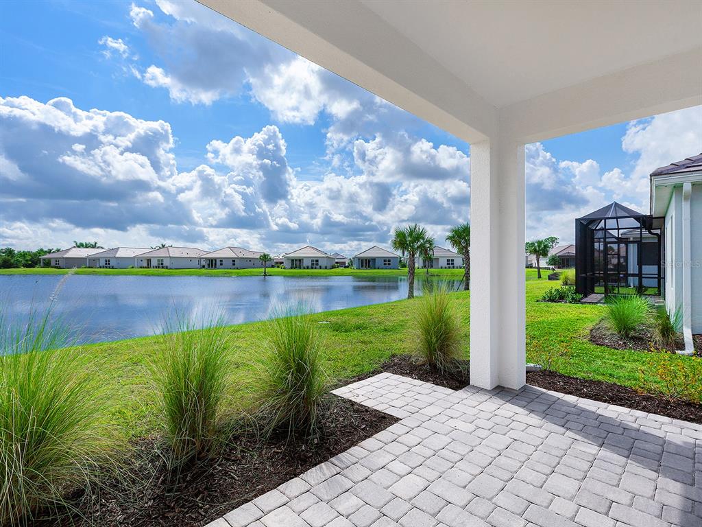 A paved patio overlooks a lake surrounded by houses under a cloudy blue sky — 18260 VIZCAYA COURT, VENICE, FL