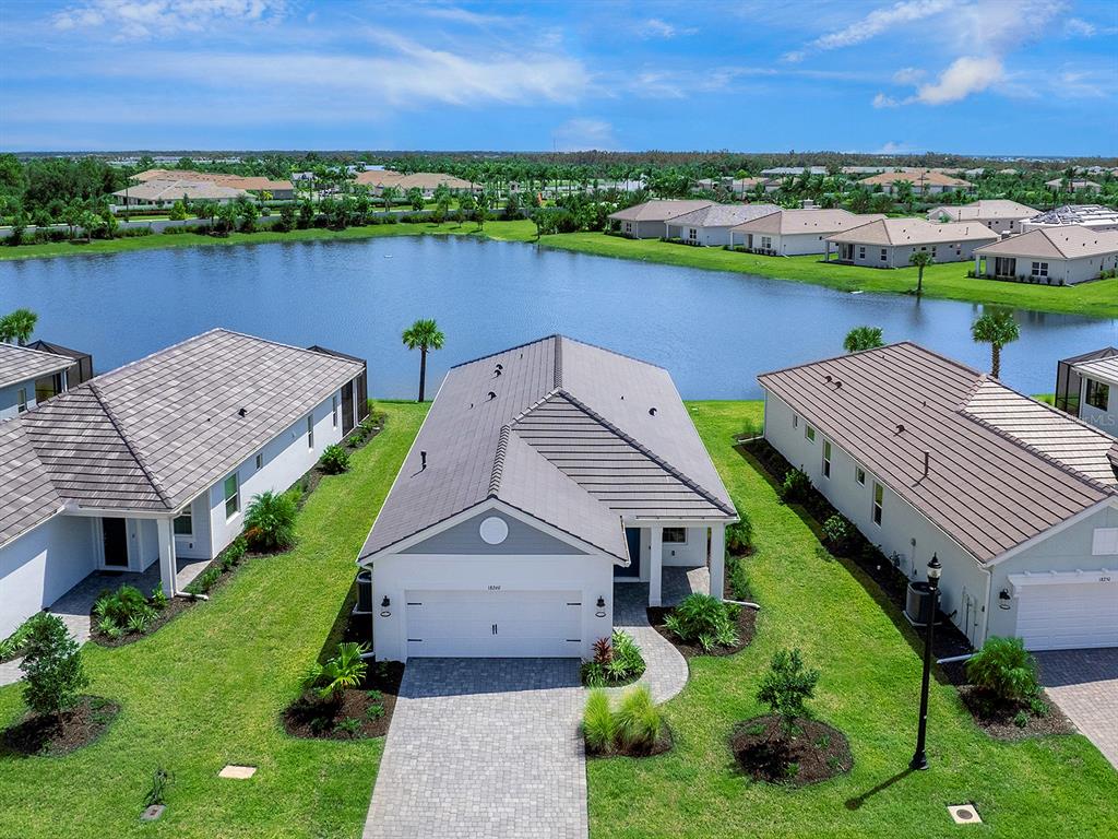 An aerial view shows a single-story house with a gray roof facing a lake — 18260 VIZCAYA COURT, VENICE, FL