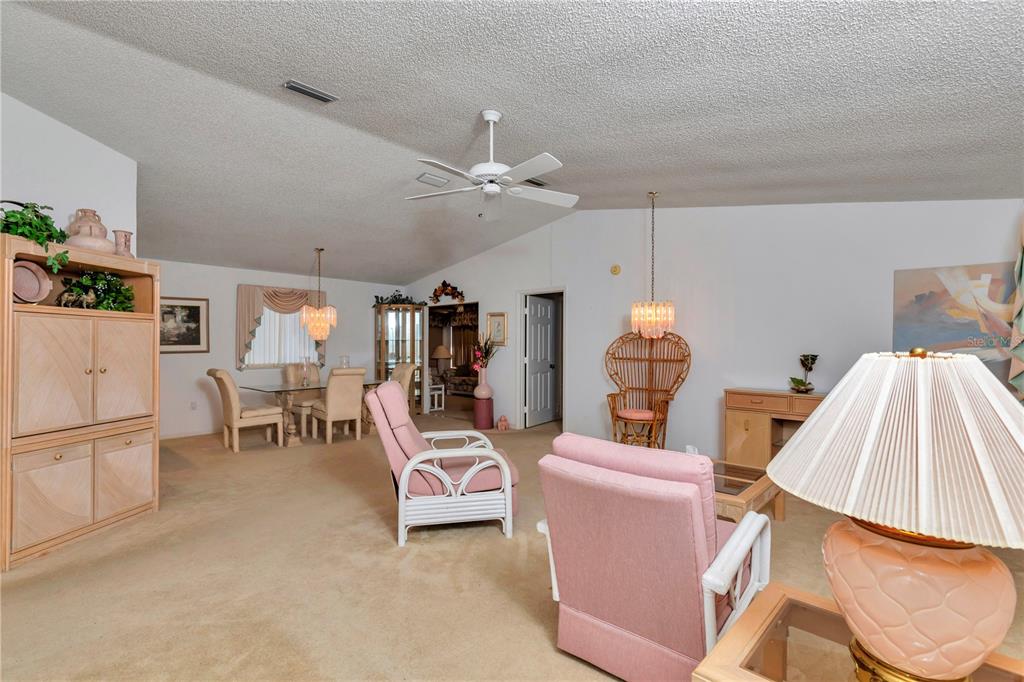 A living and dining area features beige carpeting, pink armchairs, and two crystal chandeliers — 8157 SW 108TH STREET ROAD, OCALA, FL