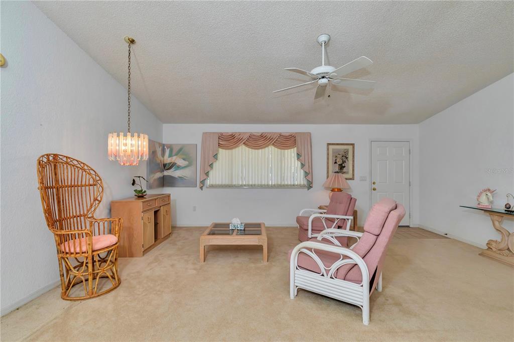 A living room features beige carpeting, a ceiling fan, wicker furniture, and a pink armchair — 8157 SW 108TH STREET ROAD, OCALA, FL