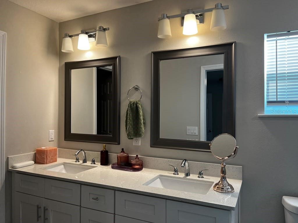 A bathroom vanity features dual sinks, dark-framed mirrors, and light gray cabinetry with quartz countertops — 15200 SW 60TH CIRCLE, OCALA, FL