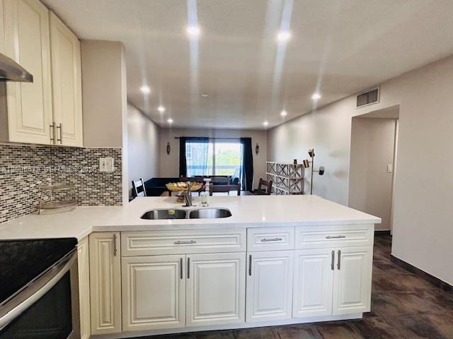 A kitchen with white cabinets, a quartz island, and a mosaic backsplash overlooks a living area — 7740 Camino Real # G404, Miami FL 33143, MIAMI, FL
