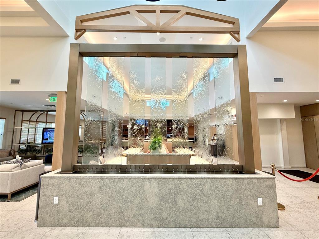 A large indoor water feature with a glass panel stands in a modern lobby area — 3151 SUNSET WALK DRIVE UNIT 112, KISSIMMEE, FL