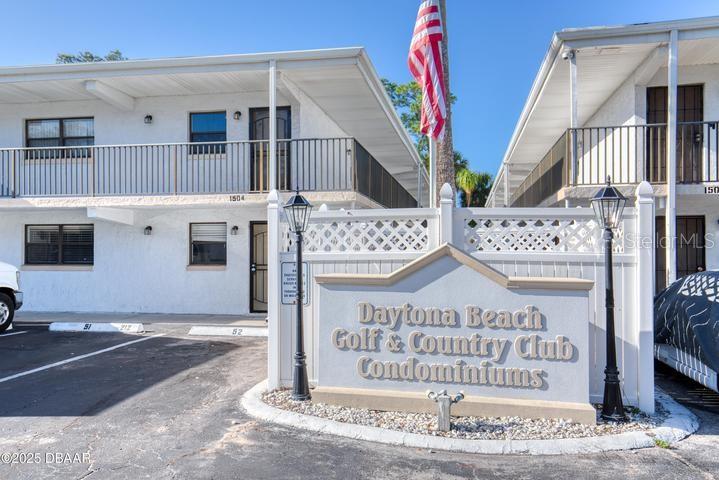 The exterior of a two-story condominium complex features a prominent monument sign and an American flag — 1504 VIRGINIA AVENUE UNIT 101, DAYTONA BEACH, FL