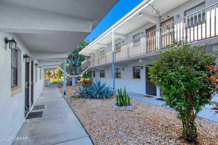 A two-story apartment building exterior features a concrete walkway, gravel landscaping, and metal railings — 1504 VIRGINIA AVENUE UNIT 101, DAYTONA BEACH, FL