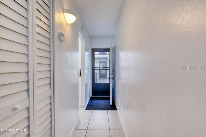 A hallway with white walls, tiled floors, a louvered closet door, and a glass-paneled door — 1504 VIRGINIA AVENUE UNIT 101, DAYTONA BEACH, FL