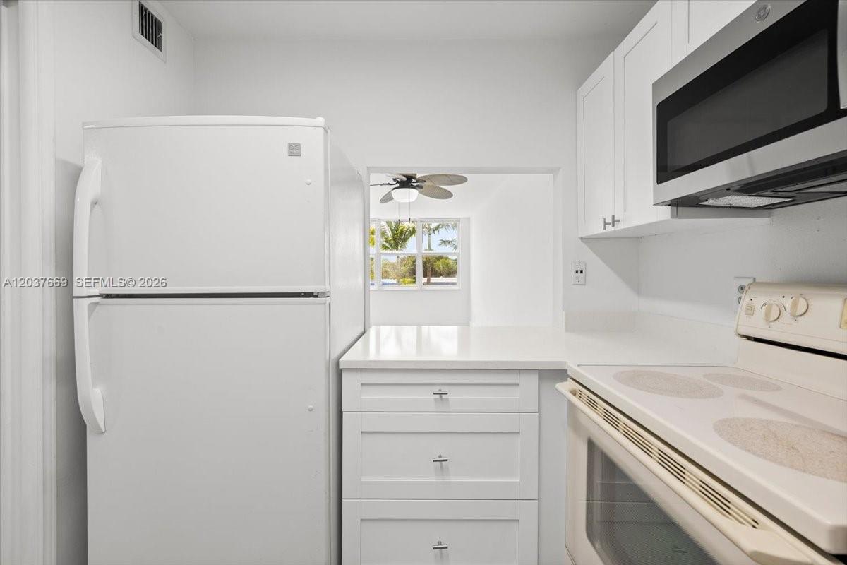 A white kitchen features a refrigerator, stove, microwave, and cabinets with a pass-through window — 9441 Evergreen Pl # 206, Davie FL 33324, DAVIE, FL