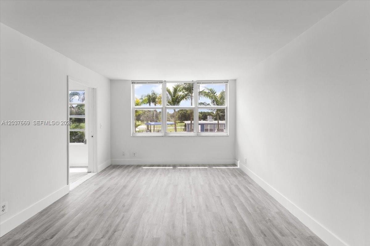 A bright, empty room features light wood-look flooring, white walls, and a large three-pane window — 9441 Evergreen Pl # 206, Davie FL 33324, DAVIE, FL