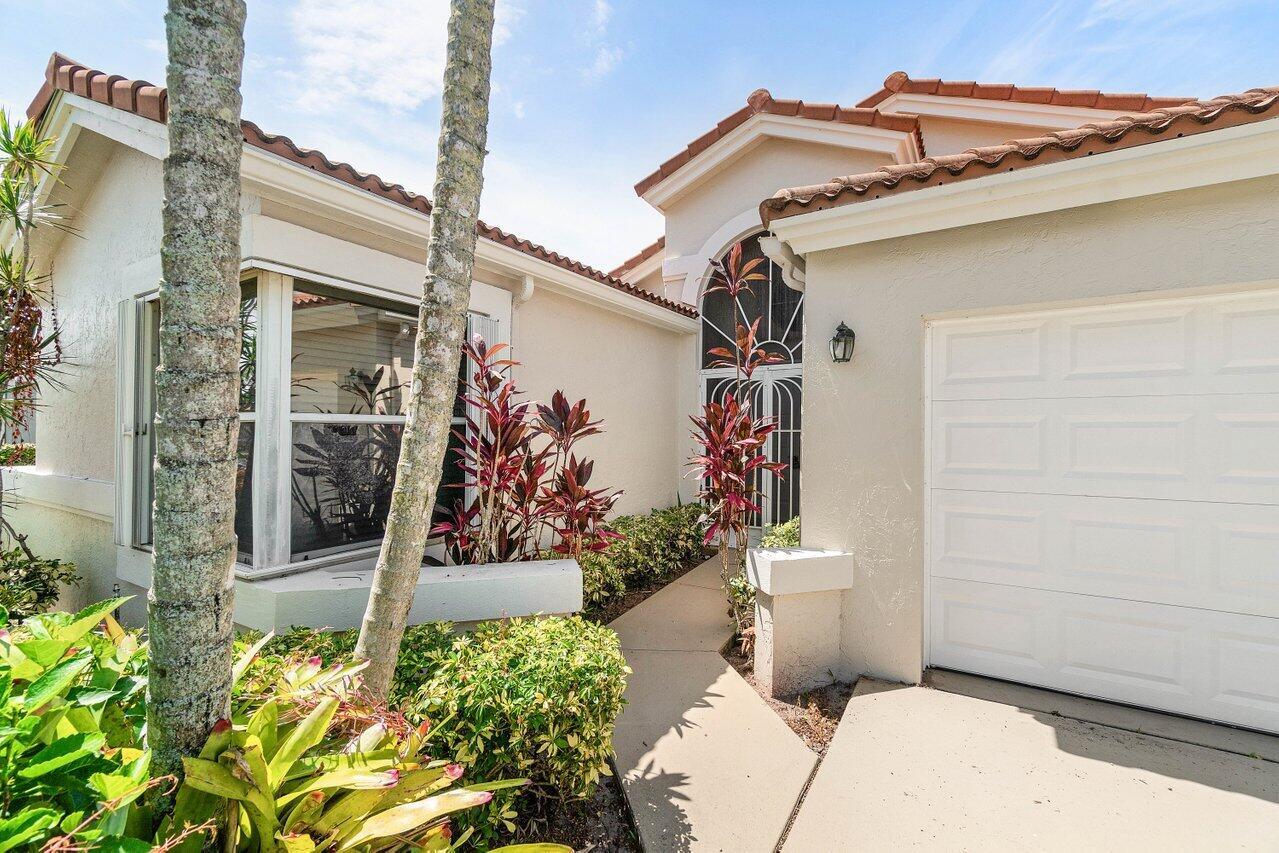 A beige house exterior features a white garage door, a walkway, and tropical landscaping — 9763 Harbour Lake Circle S, Boynton Beach FL 33437, BOYNTON BEACH, FL