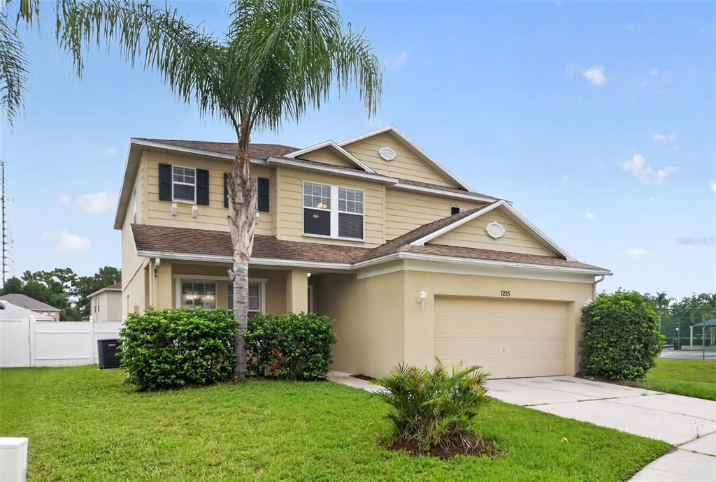 A two-story house with tan siding, a stucco garage, and a palm tree in the yard — 1215 ALAPAHA LANE, ORLANDO, FL