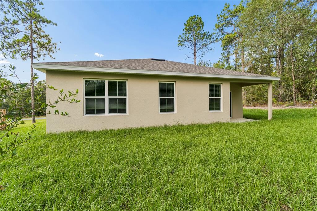 The exterior rear view of a single-story beige house with a covered patio and lawn — 1591 DOLORES, DUNNELLON, FL