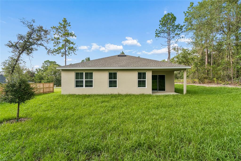 The exterior rear view of a single-story house with a covered patio and grassy yard — 1591 DOLORES, DUNNELLON, FL