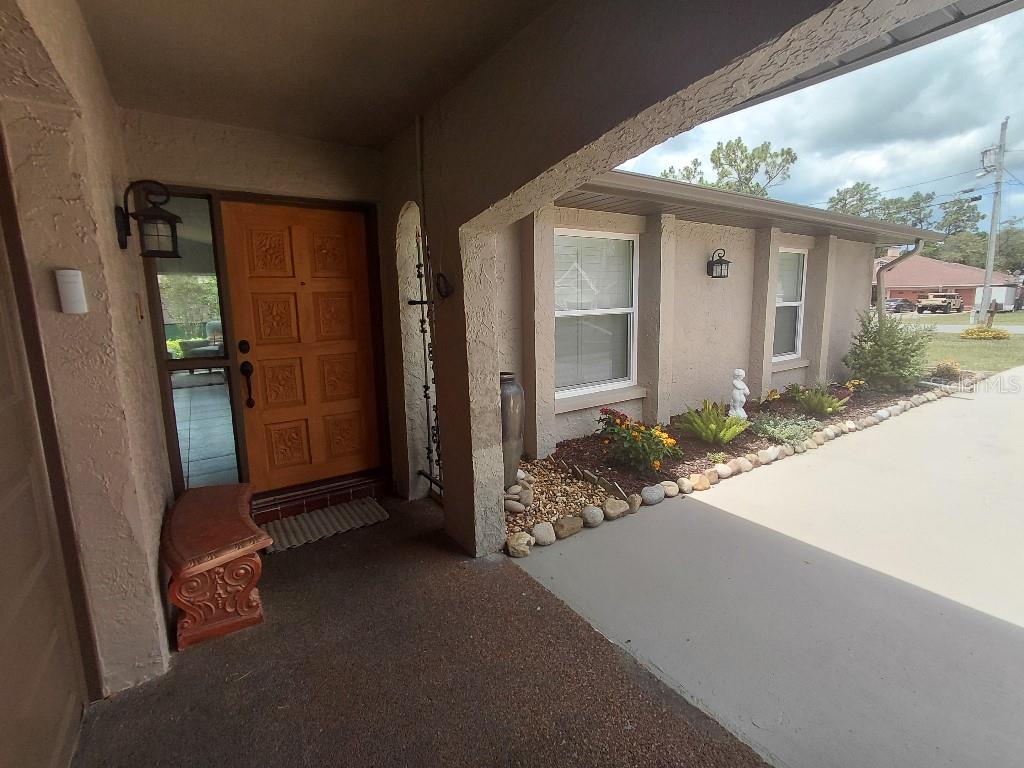 A covered entryway features a wooden front door, a concrete porch, and a landscaped garden bed — 11238 KODIAK WREN ROAD, WEEKI WACHEE, FL