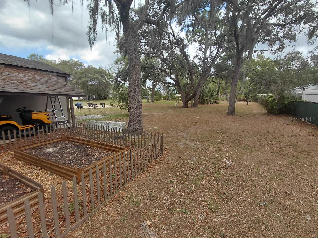 A backyard features a wooden garden bed, a lawn mower under a shed, and large trees — 11238 KODIAK WREN ROAD, WEEKI WACHEE, FL