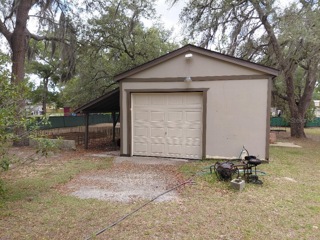 A detached garage with a side carport sits on a grassy lot with trees — 11238 KODIAK WREN ROAD, WEEKI WACHEE, FL