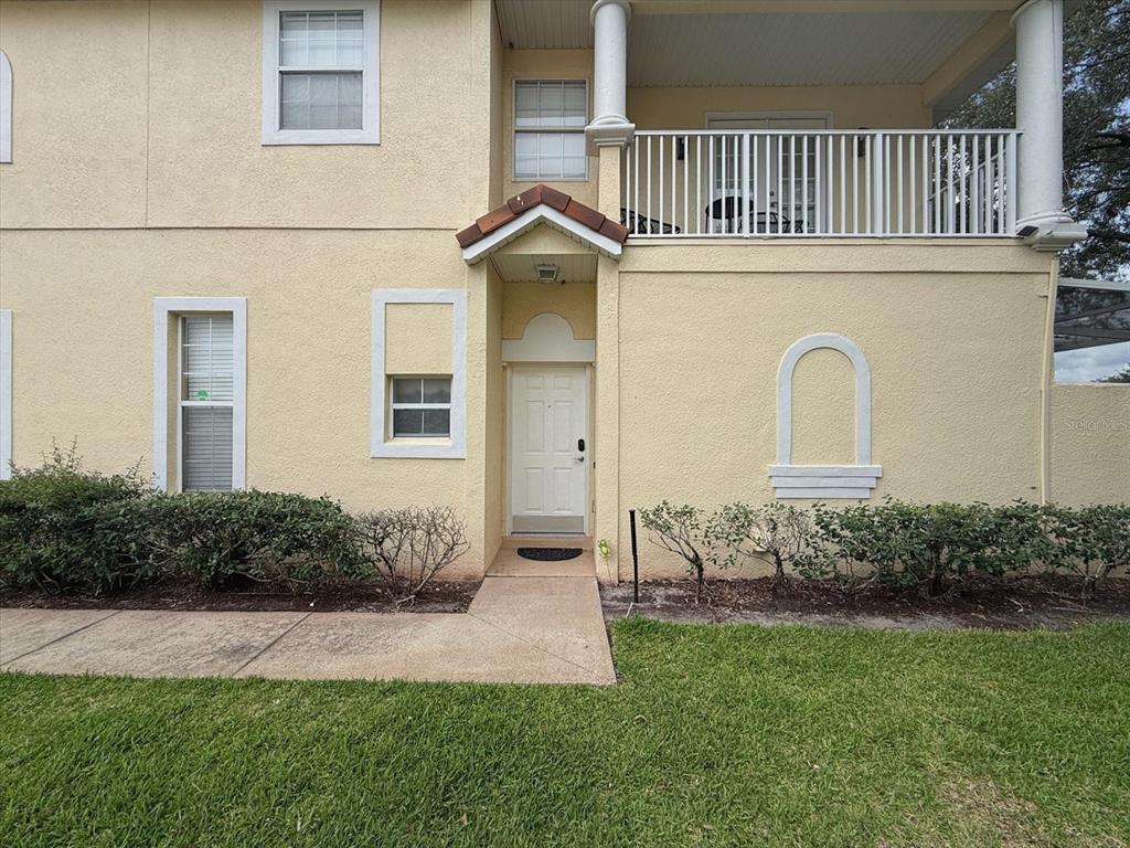 A two-story beige stucco building features a second-floor balcony, a white front door, and landscaping — 1302 S BEACH CIRCLE, KISSIMMEE, FL