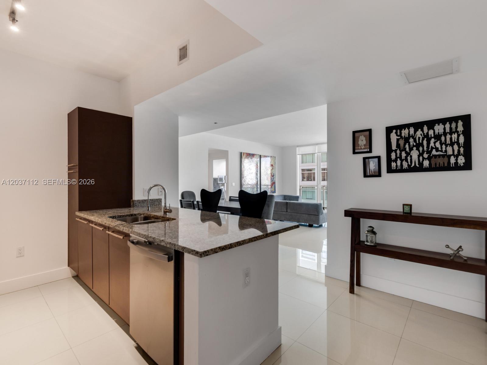 A modern kitchen with granite countertops and stainless steel appliances opens into a living area — 950 Brickell Bay Dr # 1404, Miami FL 33131, MIAMI, FL