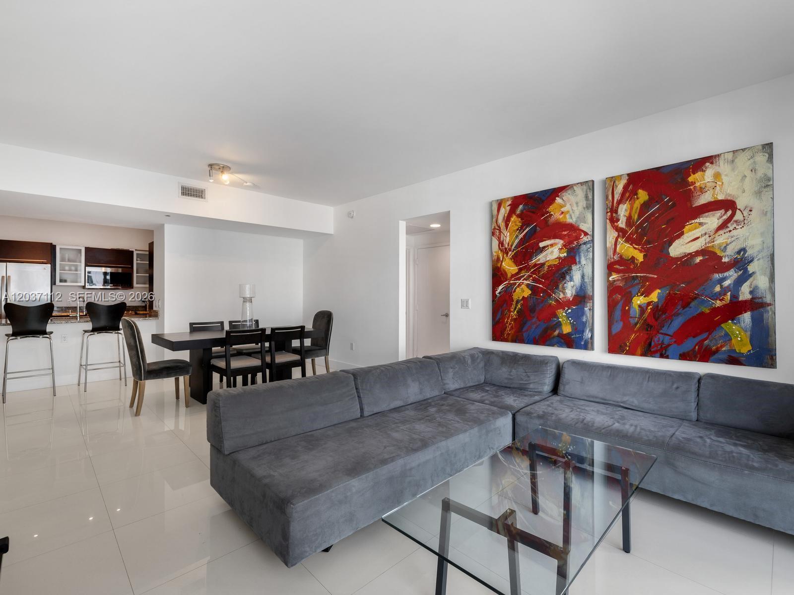 A modern living and dining area features a grey sectional sofa, glass table, and artwork — 950 Brickell Bay Dr # 1404, Miami FL 33131, MIAMI, FL