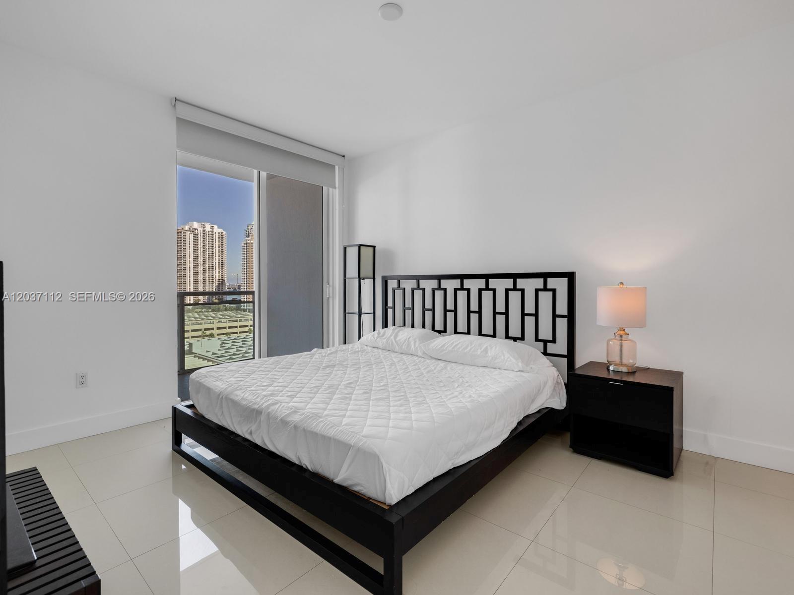 A bedroom features a black bed frame, a white quilt, and a balcony with city views — 950 Brickell Bay Dr # 1404, Miami FL 33131, MIAMI, FL