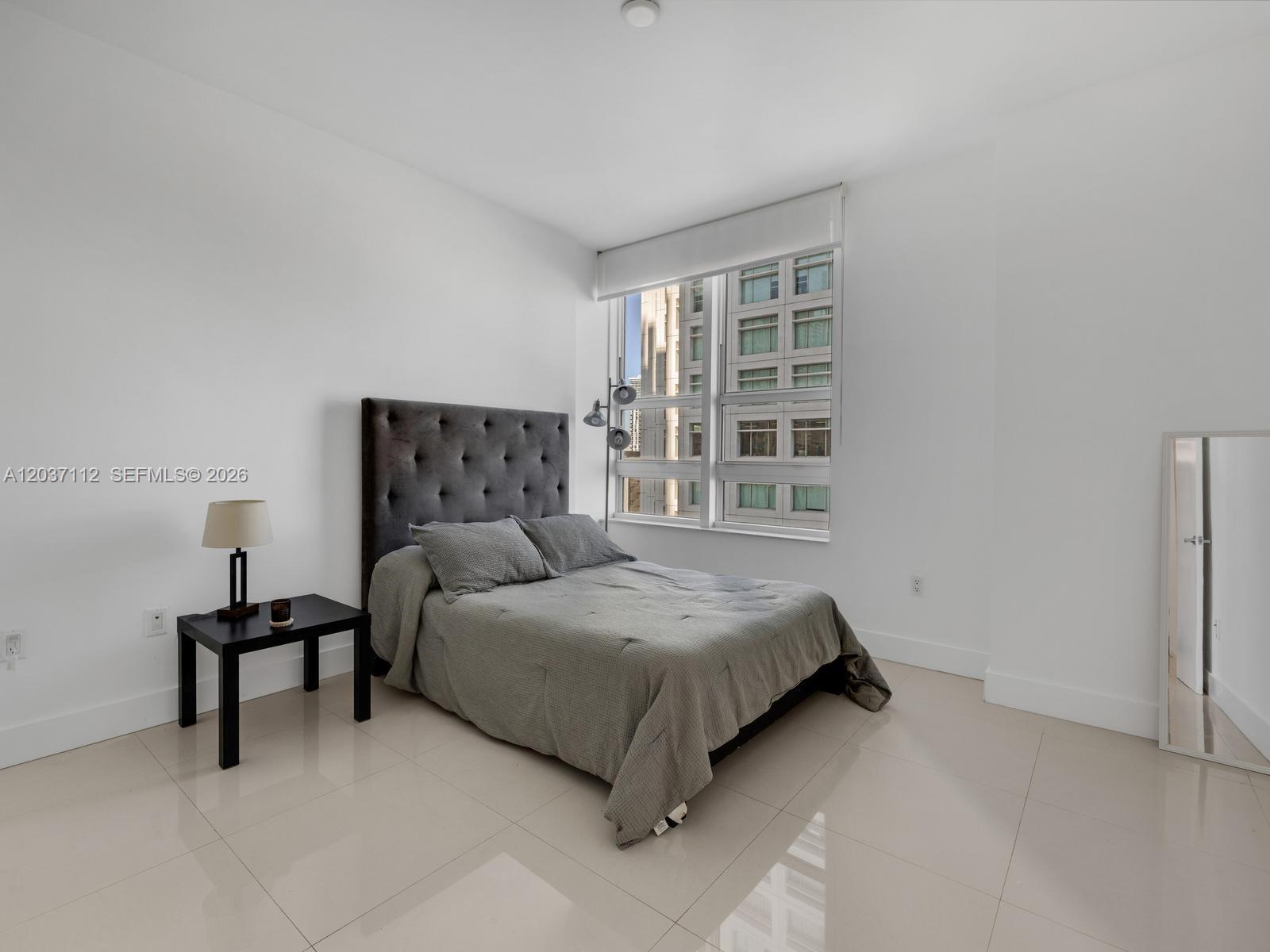 A bedroom with white walls, tile flooring, a tufted headboard, and a large window — 950 Brickell Bay Dr # 1404, Miami FL 33131, MIAMI, FL