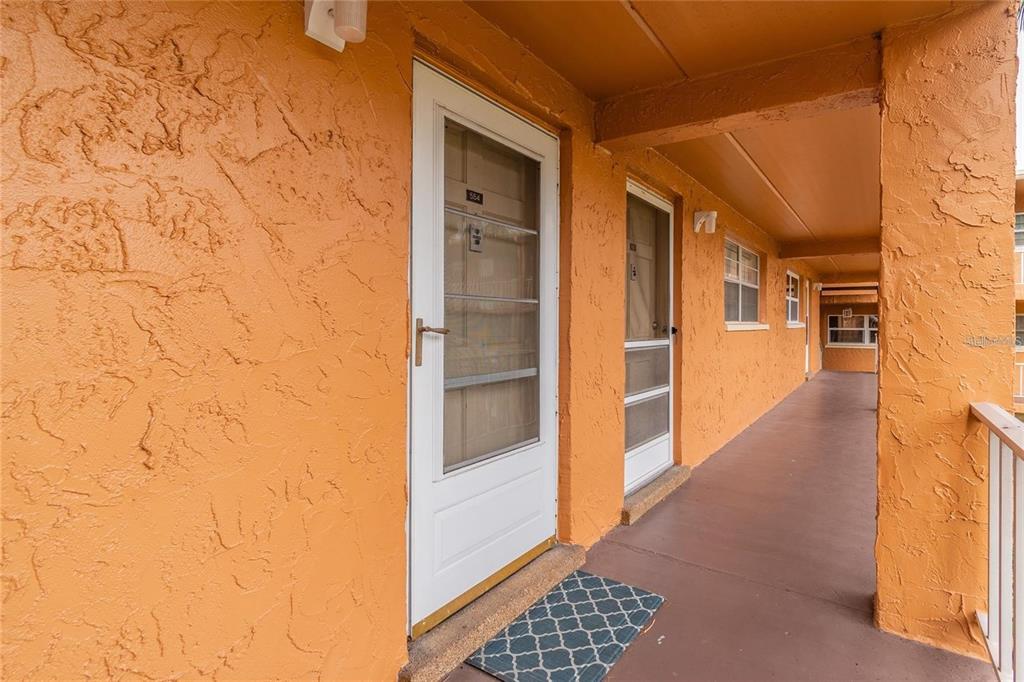 An exterior view of an apartment building walkway with orange stucco walls and white doors — 12760 INDIAN ROCKS ROAD UNIT 553, LARGO, FL