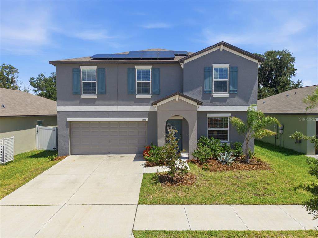 A two-story gray house features a two-car garage, solar panels, and a front entryway — 13380 GREAT PLAINS DRIVE, RIVERVIEW, FL
