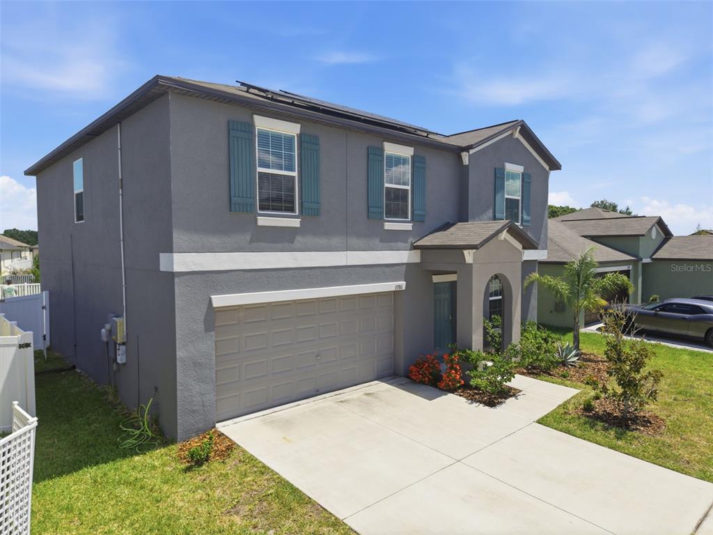 A two-story gray house with a two-car garage and teal shutters under a blue sky — 13380 GREAT PLAINS DRIVE, RIVERVIEW, FL
