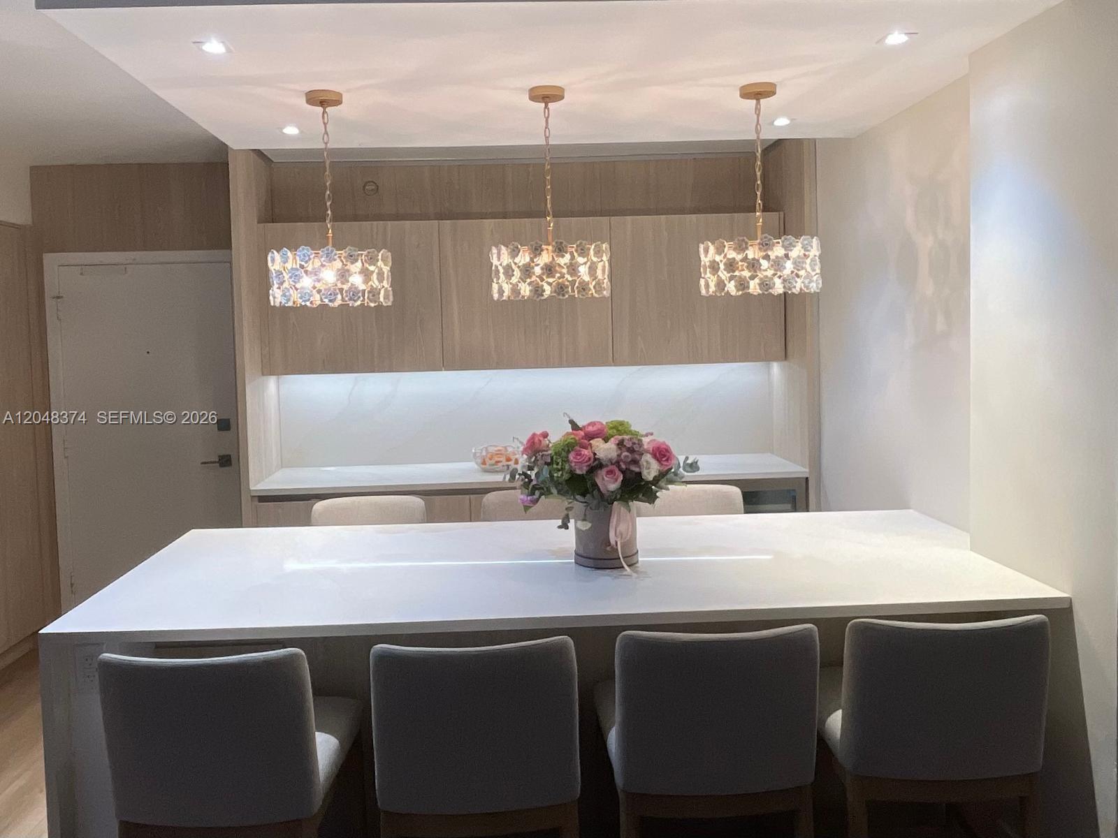 A kitchen island with four chairs sits in front of cabinetry and three pendant lights — 10275 Collins Ave # 333, Bal Harbour FL 33154, BAL HARBOUR, FL