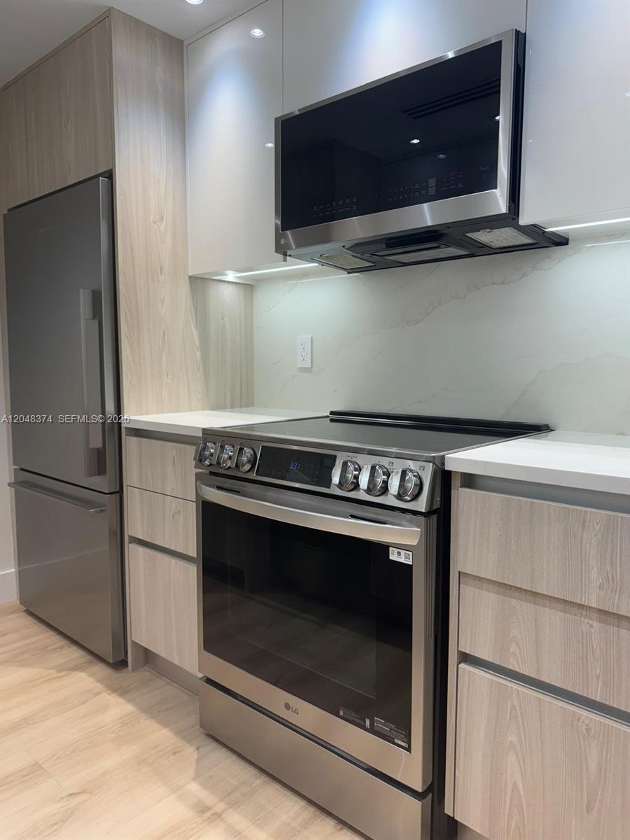 A modern kitchen features stainless steel appliances, light wood cabinetry, and a white stone backsplash — 10275 Collins Ave # 333, Bal Harbour FL 33154, BAL HARBOUR, FL