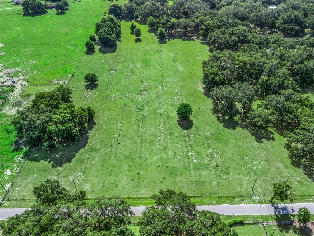 An aerial view shows a large, grassy, fenced pasture bordered by trees and a road — Lot 20 CR 543, BUSHNELL, FL