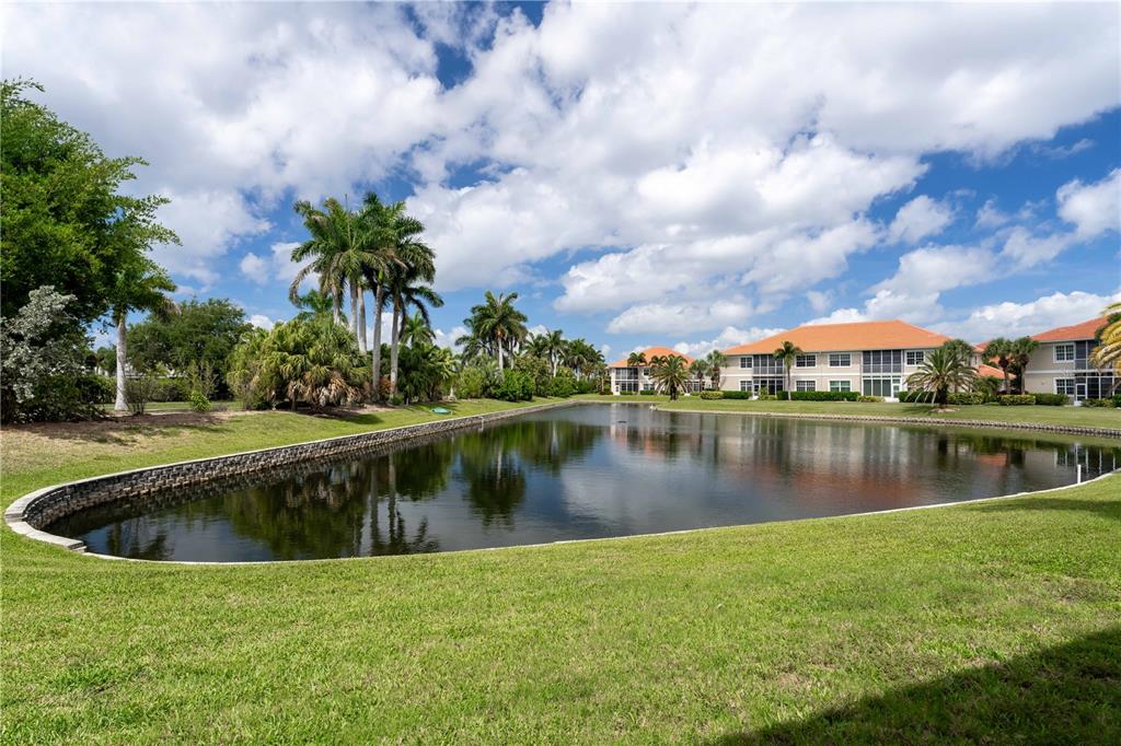 A pond sits in front of multi-story residential buildings surrounded by palm trees and grass — 197 TROPICANA DRIVE UNIT 1511, PUNTA GORDA, FL