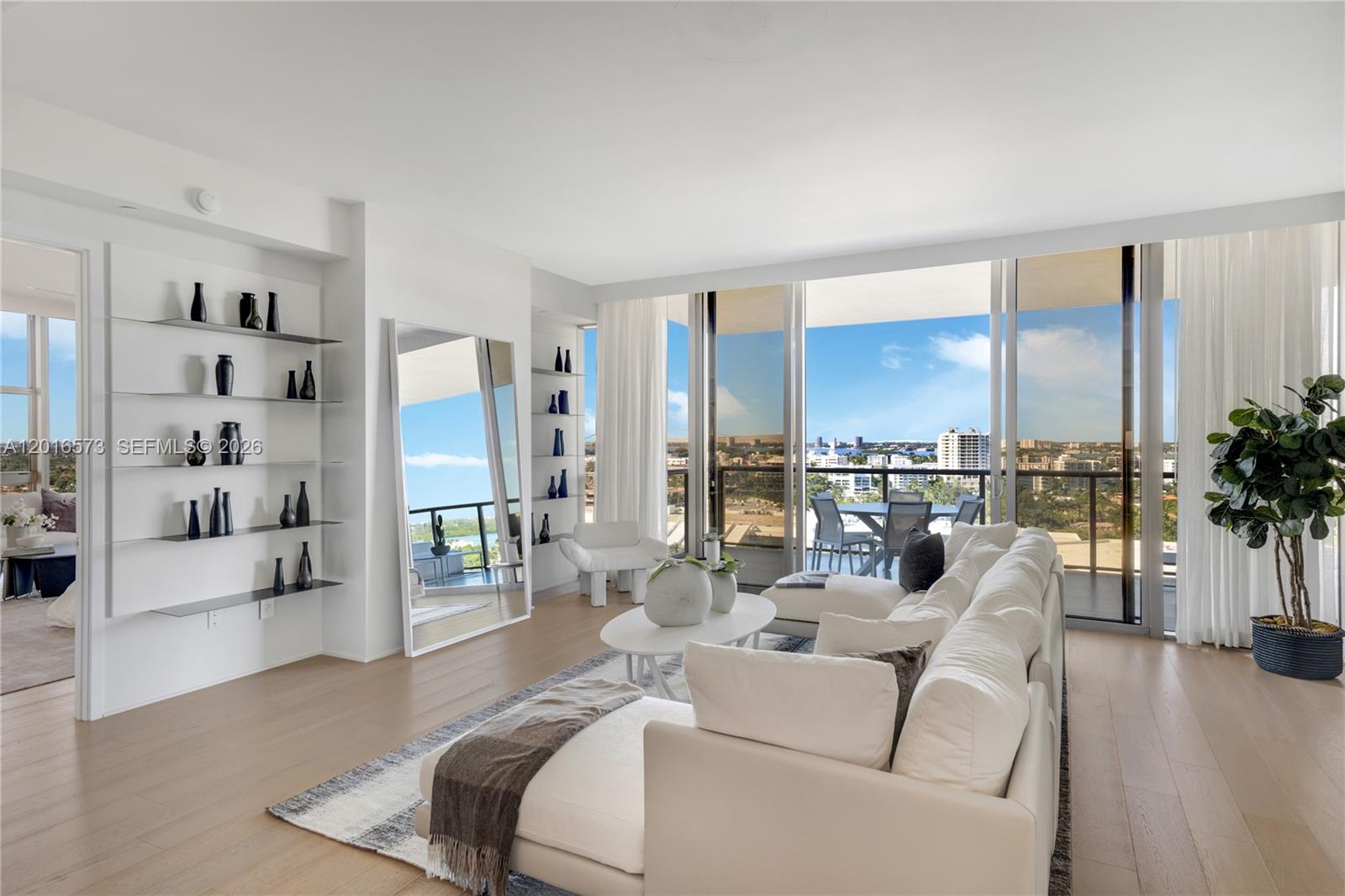A bright living room features a white sectional sofa, open shelving, and a balcony view — 9705 Collins Ave # 1205N, Bal Harbour FL 33154, BAL HARBOUR, FL