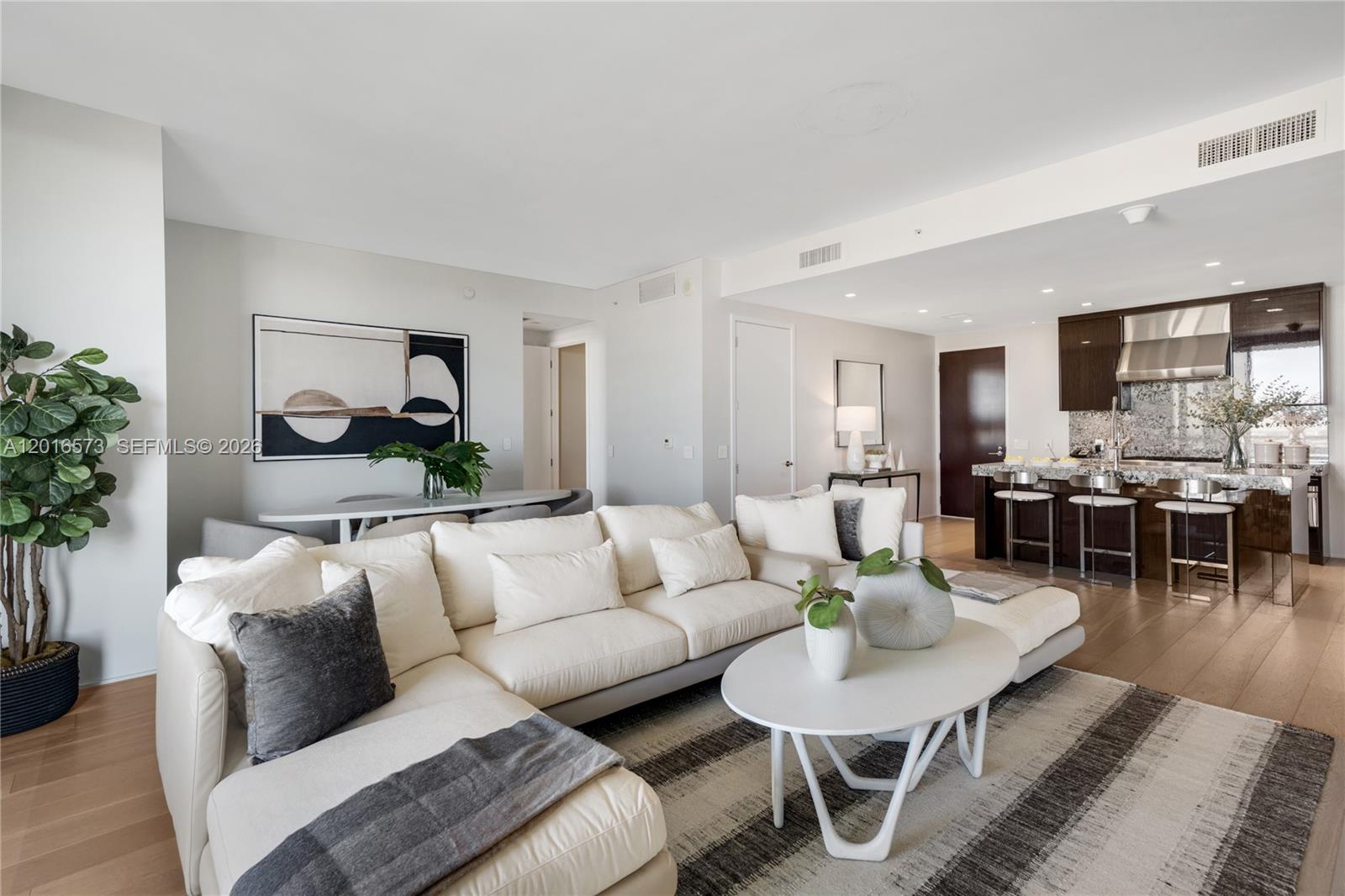 A modern living room features a white sectional sofa, a coffee table, and an open kitchen — 9705 Collins Ave # 1205N, Bal Harbour FL 33154, BAL HARBOUR, FL
