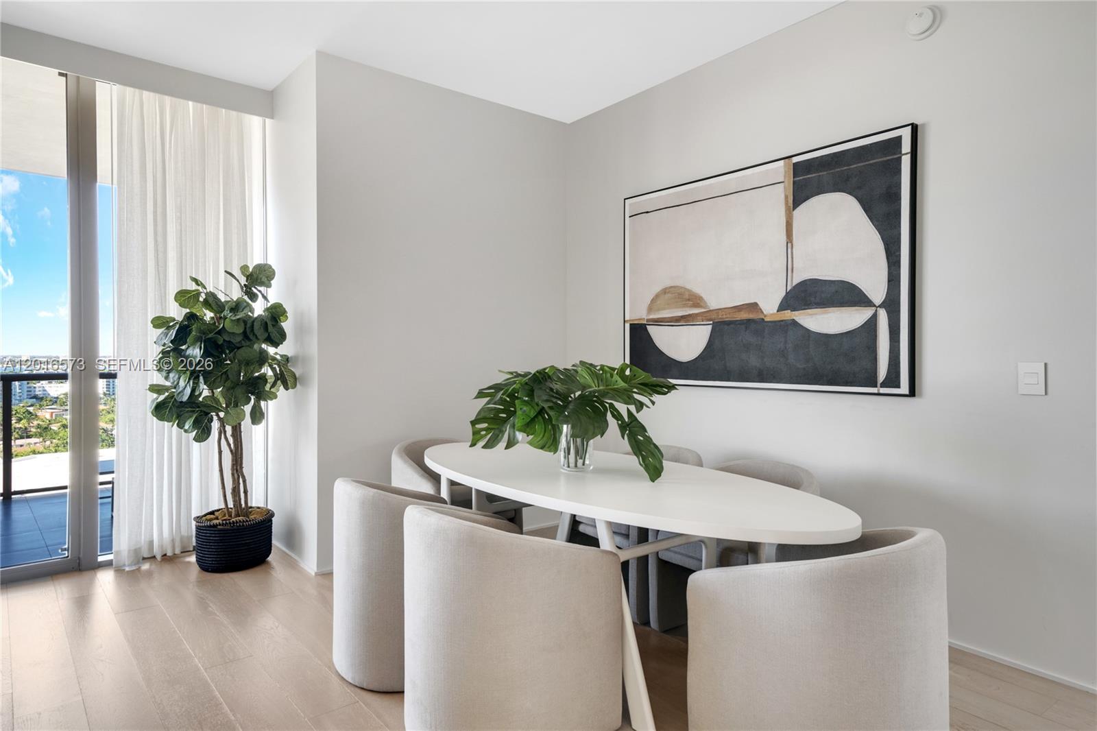 A dining area features an oval white table, upholstered chairs, a large abstract painting, and greenery — 9705 Collins Ave # 1205N, Bal Harbour FL 33154, BAL HARBOUR, FL