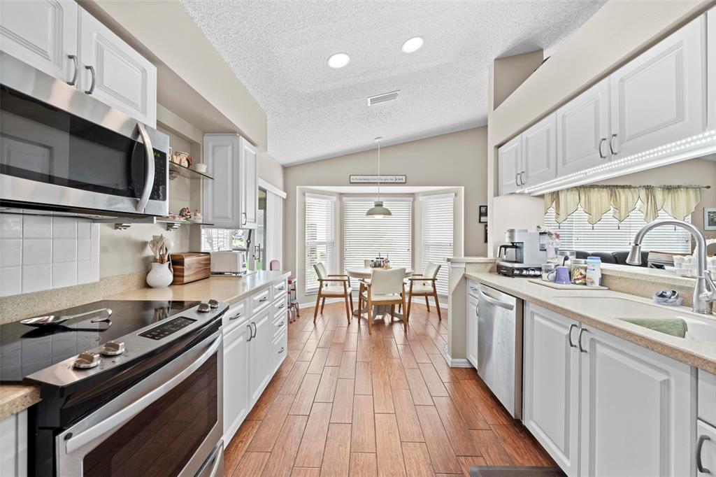 A kitchen with white cabinets, stainless steel appliances, and wood-look tile flooring leads to a dining area — 2552 CRYSTAL LAKE DRIVE, SPRING HILL, FL