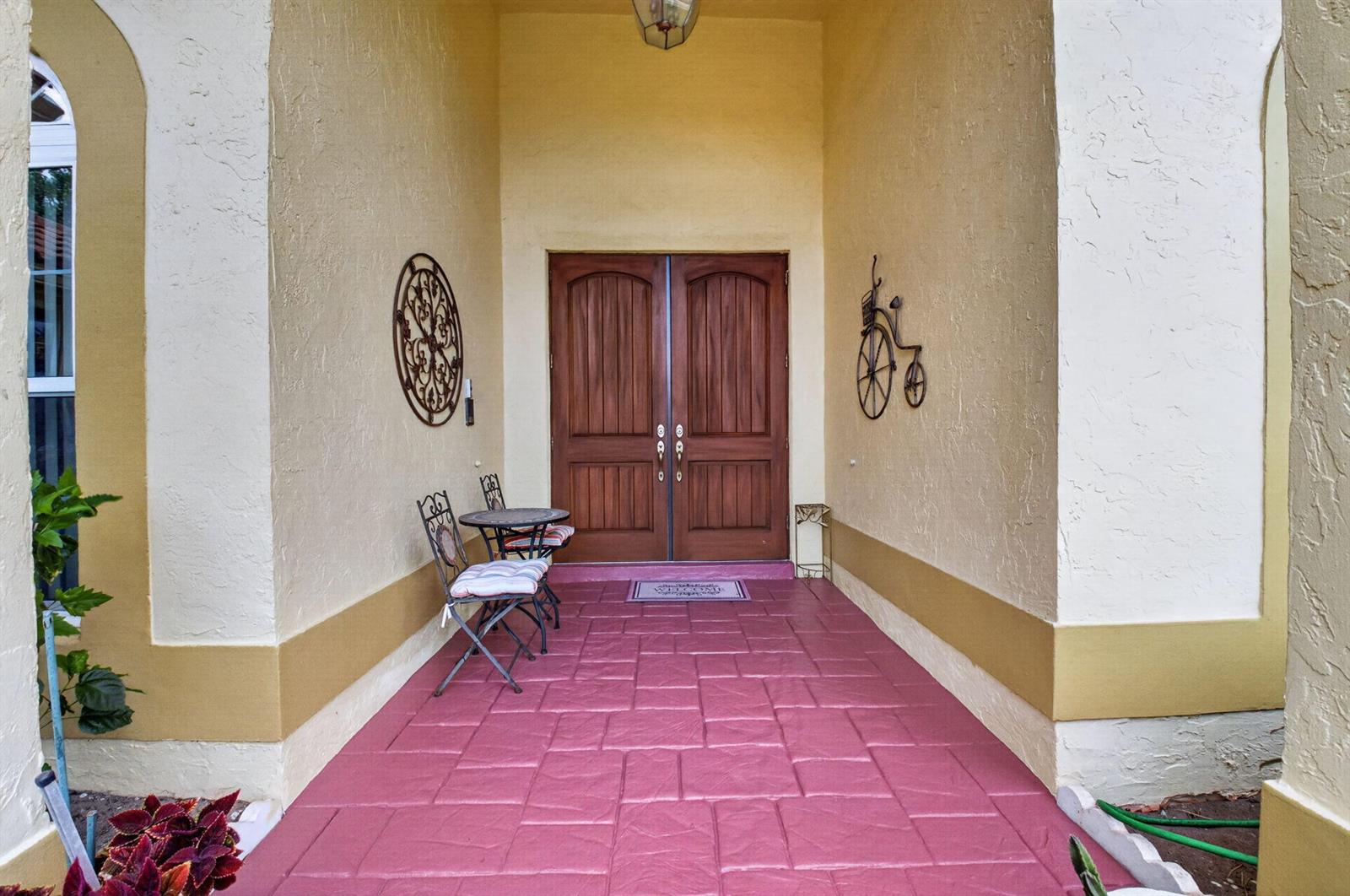 A covered entryway features double wooden doors, pink paved flooring, and a small bistro set — 2931 NW 25th Way, Boca Raton FL 33434, BOCA RATON, FL