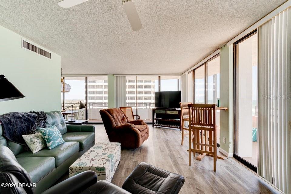 A living room features a green sofa, a brown recliner, and floor-to-ceiling windows — 2828 N ATLANTIC AVENUE UNIT 701, DAYTONA BEACH, FL